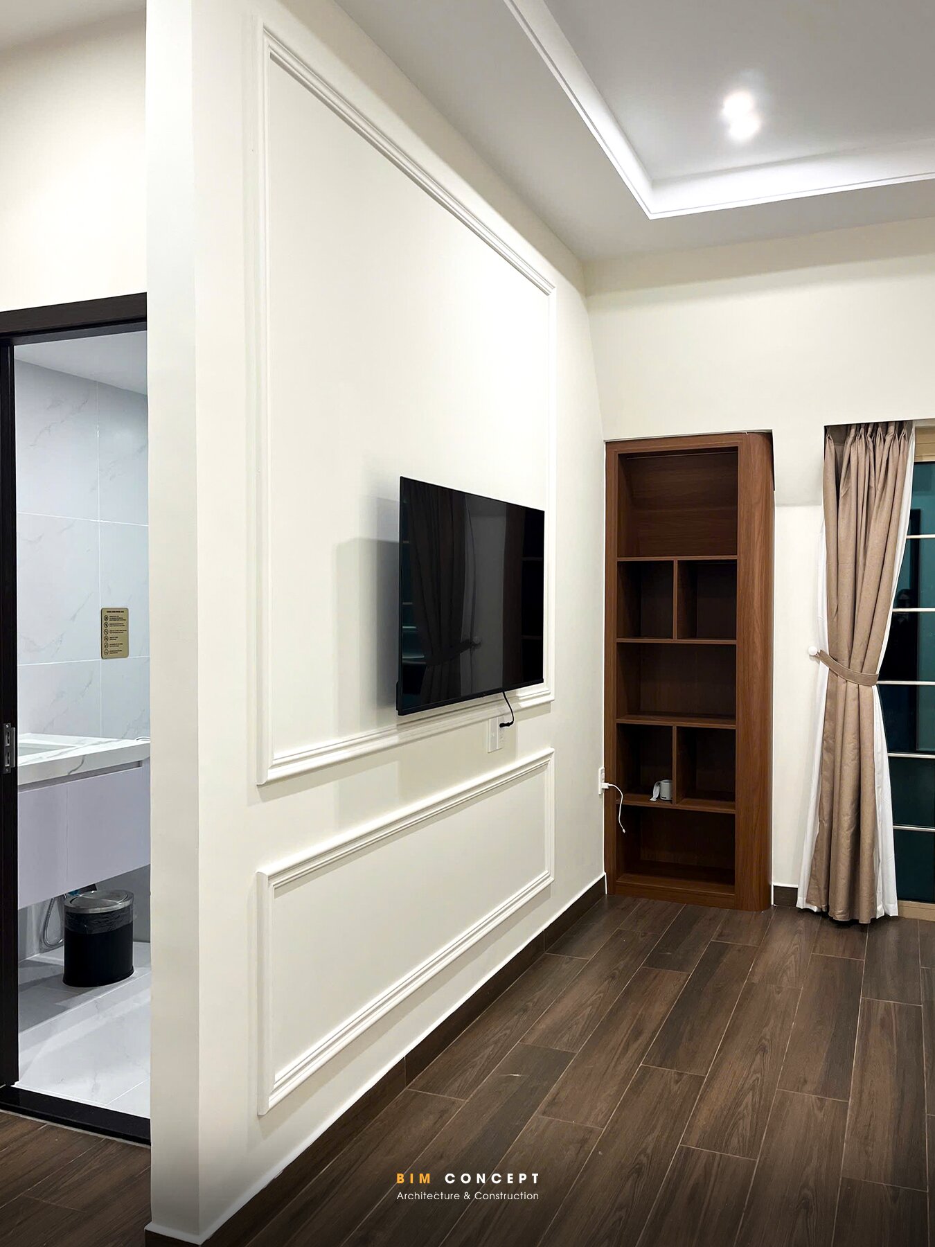 Thi công nội thất shophouse phòng ngủ có tivi treo tường và kệ gỗ âm tường.